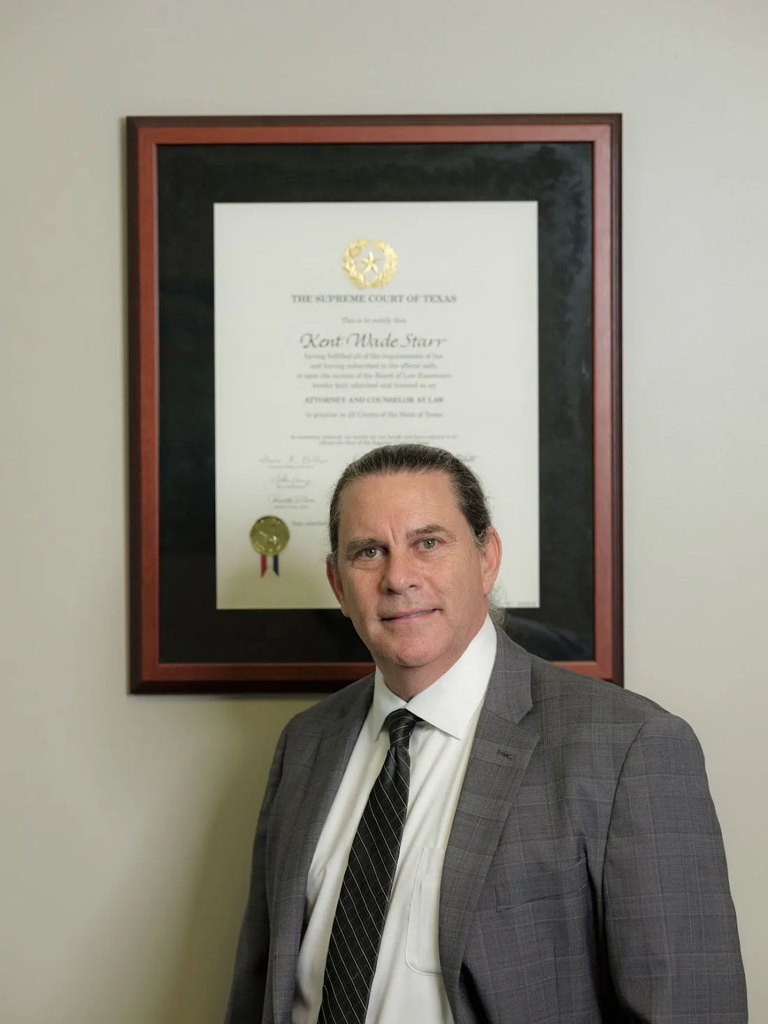 Kent Starr standing in his office, with the Texas Supreme Court attorney certificate visible behind him.